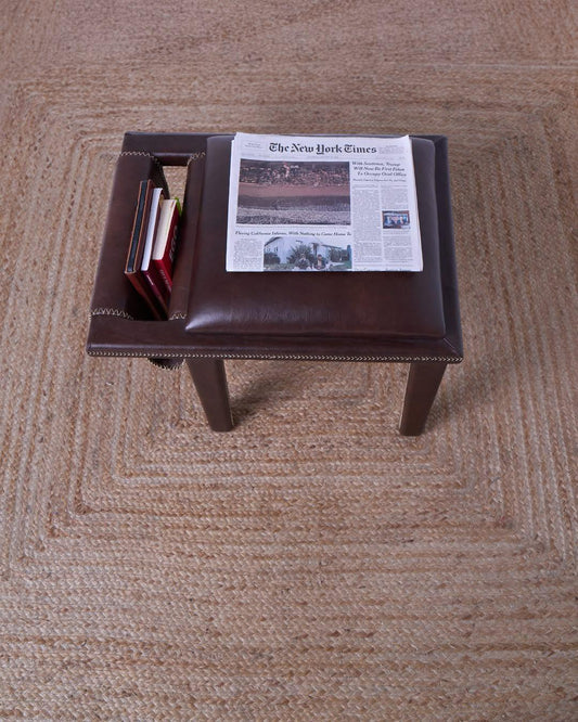 A traditional African stool with a leather seat and wooden legs, featuring a magazine on top.